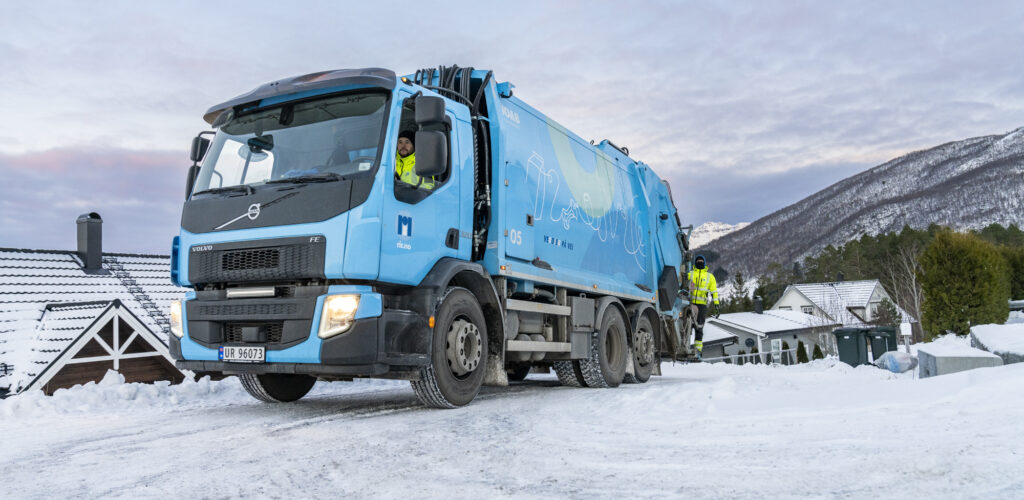 Renovasjonsbil med sjåfør og mann bakpå i vinterlandskap