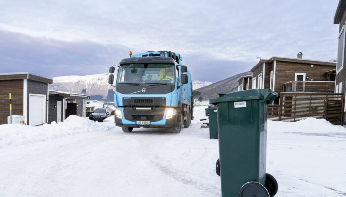 Renovasjonsbil på vei inn i boligområde, med en avfallsdunk i forgrunnen.